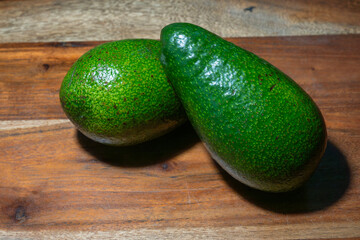 Two fresh green avocados rest side by side on a warm-toned wooden surface, radiating natural simplicity.