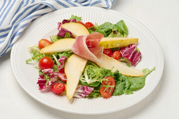 Close up of a gourmet salad with prosciutto, pear slices, cherry tomatoes and fresh mixed greens