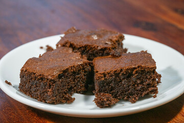Four rich, homemade chocolate brownies sit invitingly on a white plate atop a rustic wooden table.