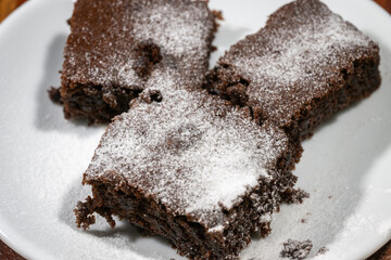 Three rich chocolate brownies dusted with powdered sugar rest on a rustic wooden surface.