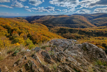 Bright autumn forest panorama from the Magos-kő peak in Hungary’s Bükk National Park, showing vibrant hills and deep valleys under a blue sky.