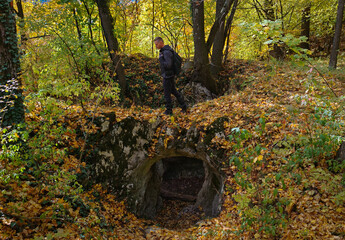 A hiker walks above the entrance of the Vidróczky Cave in the Bükk Mountains, Hungary, surrounded by colorful autumn leaves and forest light.