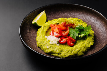Fresh avocado dip served with toppings on a dark plate