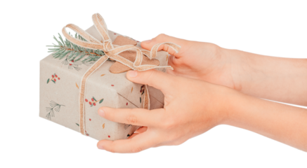 Hands holding a Christmas gift wrapped in eco kraft paper with pine branch, berries, and natural twine, isolated on white background. Sustainable holiday packaging and eco-friendly celebration concept