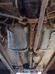 Bottom up view of a rusty old car's underside or undercarriage. Rusted underbody suspension and exhaust components, wide angle view, no people