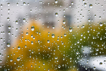 Rain drops flowing down a large home window with blurry fall colored trees in the background. Close up view, shallow depth of field, moody, no people