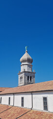 The historic Cathedral of the Assumption of the Blessed Virgin Mary in Krk, Croatia, with its distinctive bell tower and red-tiled roofs, stands against a clear blue sky