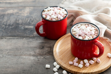 Hot chocolate drink with marshmallows in red mug on wooden table. Copy space