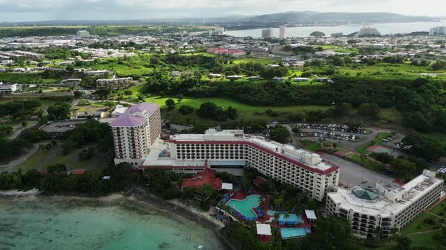Orbiting aerial view of Hilton Guam Resorts and Hotel amid tropical island scenery during daytime.