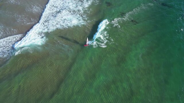 High angle drone shot following a wind surfer, surfing on the coast of Portugal