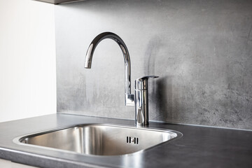 Closed, new, stainless water tap faucet and sink in apartment kitchen. Bright, natural window light, selective focus, no people