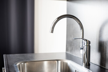 Closed, new, stainless water tap faucet and sink in apartment kitchen. Bright, natural window light, selective focus, no people