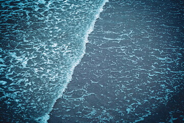 Foamy, shallow, tidal waves reaching the sandy shore. Top down view, shallow water, aqua blue cold tones, no people