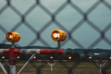 Precision Approach Path Indicator lights in front of an empty airport runway strip and edge lights. Close up shot of the light clusters, dark, moody, cloudy atmosphere, no people