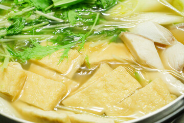 A stewed hot pot dish featuring mizuna greens, green onions, mackerel, and fried tofu—a Japanese winter delicacy.