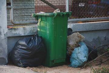 Full green bin surrounded by bulging black and blue trash bags.