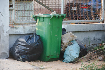 Full green bin surrounded by bulging black and blue trash bags.
