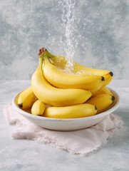 Fresh Bananas in Bowl with Water Splash on Gray Background