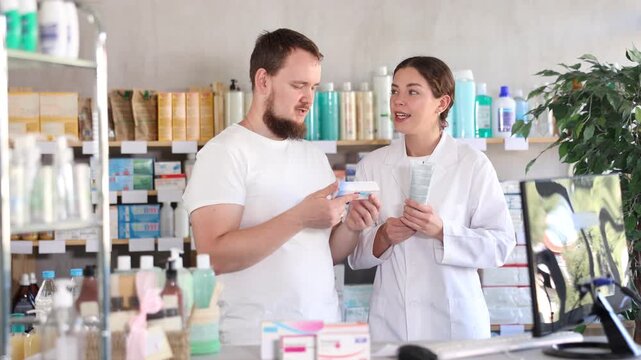 Man chooses ointment in modern pharmacy. Female pharmacist helps with choosing a medicine. High quality 4k footage