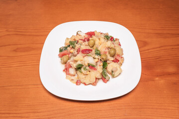A typical Spanish salad with boiled potatoes, olives, boiled eggs, and chopped tomatoes on a white plate