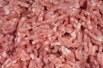 A horizontal close-up shot of raw, light pink ground pork, showing the texture of the finely minced meat and small pieces of fat