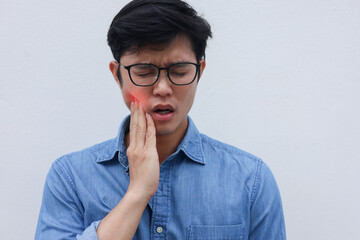 close up young asian man frown and use hand to massage on cheek after feeling pain or hurt from tmj...