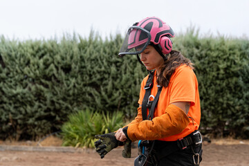 Woman arborist preparing for tree pruning, putting on safety gloves and wearing protective equipment