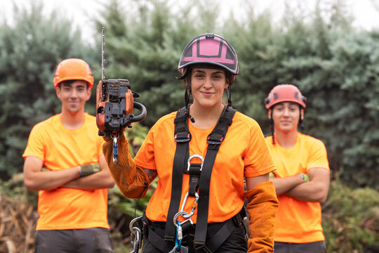 Arborist woman holding chainsaw, working with team, demonstrating confidence in tree care profession