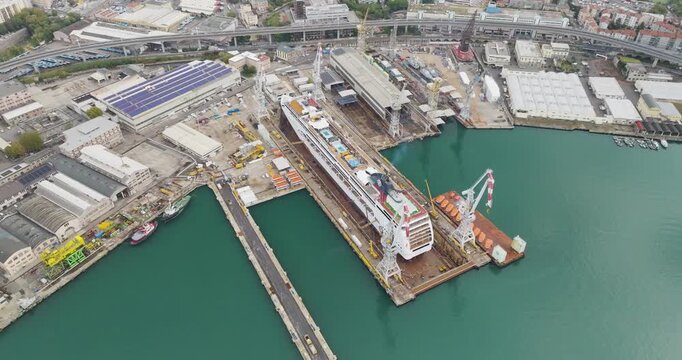 Aerial view of a massive cruise ship undergoing maintenance in a dry dock, surrounded by the industrial landscape and the deep blue waters, Trieste, Friuli-Venezia Giulia, Italy.