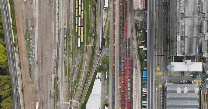 Aerial view of a complex train yard with parallel tracks and parked train cars exhibiting various colors, set against industrial buildings, Trieste, Friuli-Venezia Giulia, Italy.