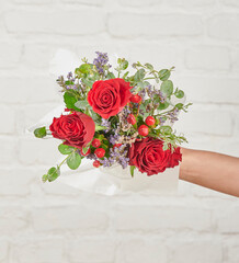 Beautiful floral arrangements: a hand-held bouquet of orange and white roses, and a pink tulip arrangement in a decorative striped box against a white brick wall.