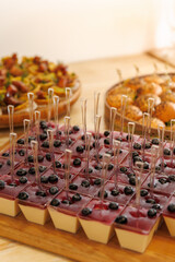 Individual panna cotta desserts with berry sauce and blueberries served in clear cups with spoons, gourmet presentation on wooden table at elegant