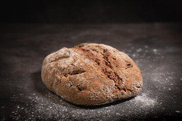 Rustic whole grain walnut bread on floured dark slate surface
