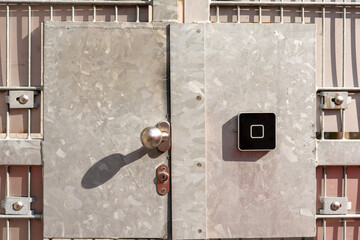 Heavy metal gate with steel plate, door knob and security lock, and a black electronic access control device.