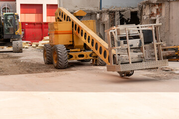 Mobile elevating work platform (MEWP), on a construction site with a teardown building and an excavator in the background. Sunlite stripe in the foreground. White space.