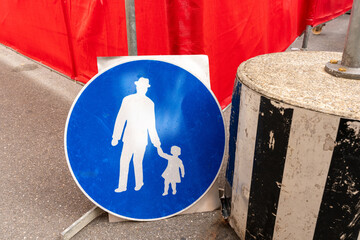 Construction site fencing, with blue foot path sign leaning against the red barrier, round concrete block with sign pole close by.