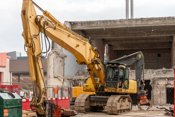 Excavators in front of a demolition house. In the foreground a big one with a hydraulic crusher, a smaller one with grabber in the background.