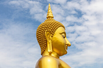 Side profile of the Great Buddha statue at Wat Muang temple in Ang Thong, Thailand, showing the golden serenity and peaceful expression under a bright blue sky.