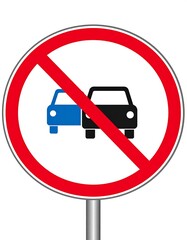 A circular road sign displaying two car silhouettes, one blue and one black, crossed by a red diagonal line indicating a restriction