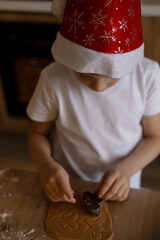 Little boy preparing gingerbread cookies at kitchen with Christmas decorations. Kid's hands cutting ginger dough with cutter to making cookies for winter holidays