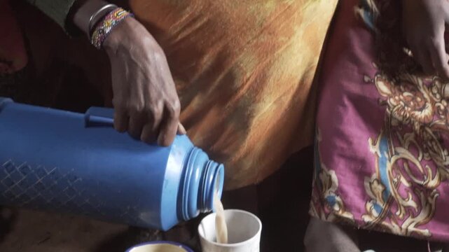 Pouring aromatic hot masala chai or tea from a blue flask/thermos into cups.