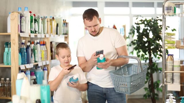 Dad and son scan barcode on packaging of mouthwash, looking for information about product on website. Boy watches actions of dad, learns to scan QR code using phone camera