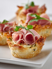 food photography, one mini phyllo quiche with lot of fresh turkey ham slices on a white background, 