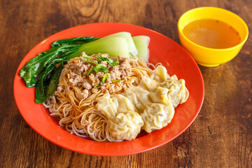 Wonton noodles – nouilles fines malaisiennes avec leurs ravioles farcies, présentées dans une assiette colorée sur table en bois