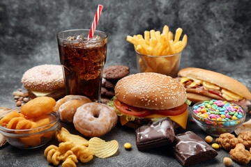 Assortment of fast food and sugary snacks including burger fries donuts chocolate and soda on gray background