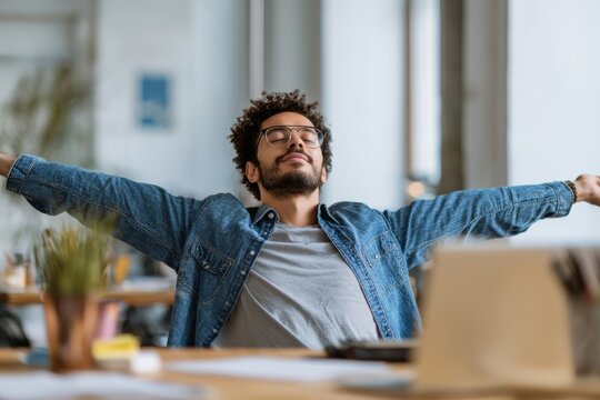 Man stretching arms at desk after long work session, expressing relief and satisfaction.