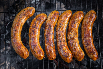 Rack of hot dogs are cooking on a grill. The hot dogs are brown and have a lot of seasoning on them