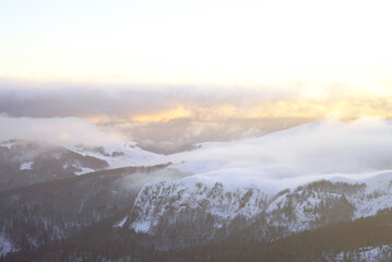 An atmospheric landscape from the Kolašin ski resort at 1600: low clouds, illuminated by the setting sun, drifting over snow-capped mountains. Inspiration for winter travel. A visit to Mount Bjelasica