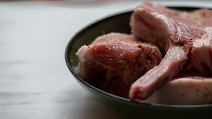Raw marinated pork ribs in a green bowl on a kitchen table