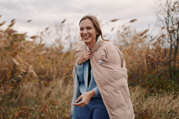 Authentic portrait of a woman outdoors in autumn, wearing a warm puffer and denim, smiling as natural light highlights true expression and simple style.